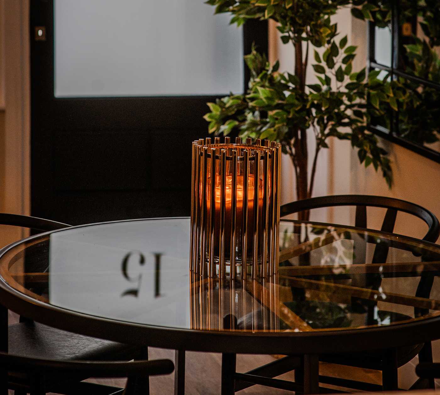 A gold cylindrical candle holder on a round glass dining table with dark chairs - a styling detail from the Coastal Residence by Atlantic Interiors