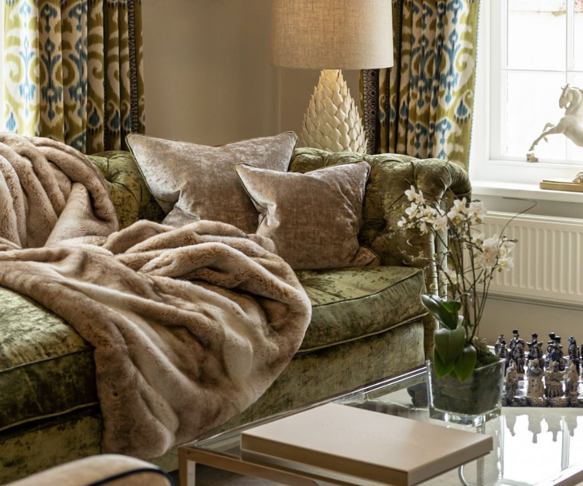 A luxury residential lounge with a green velvet sofa, faux fur throw, ikat patterned curtains and a large table lamp - interior design by Atlantic Interiors